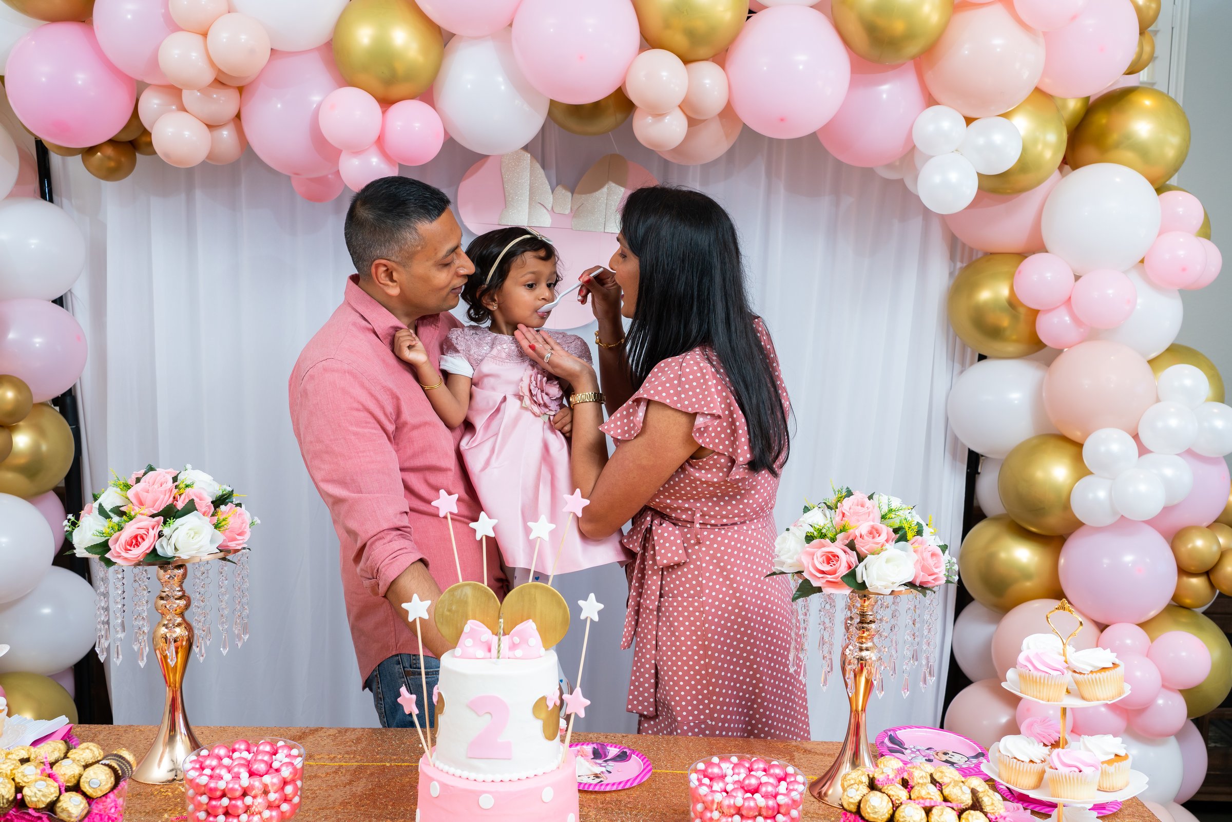 Krisha 2nd birthday parents feeding cake under arch