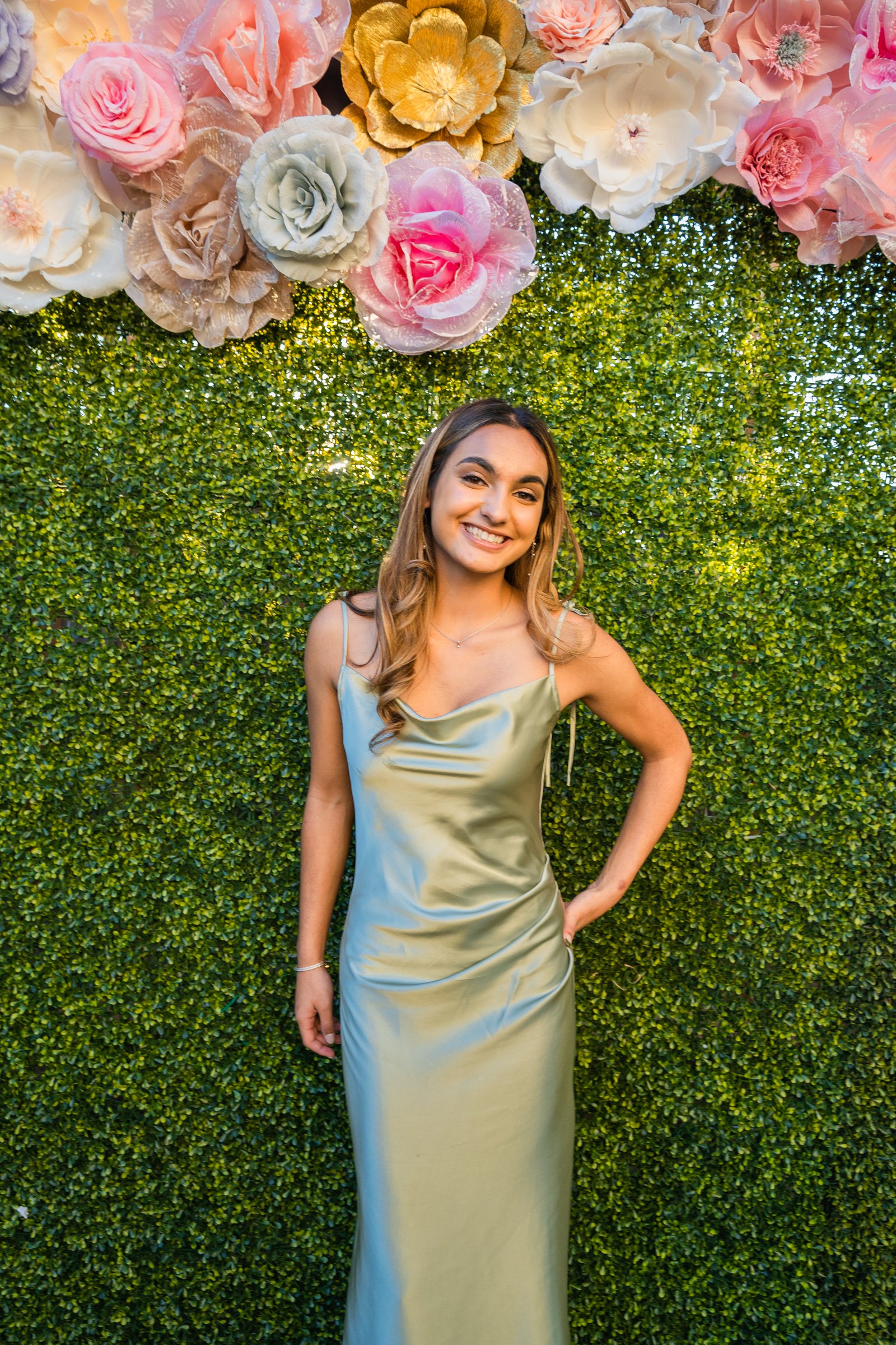 Ria's sweet 16 sage gown against flower wall